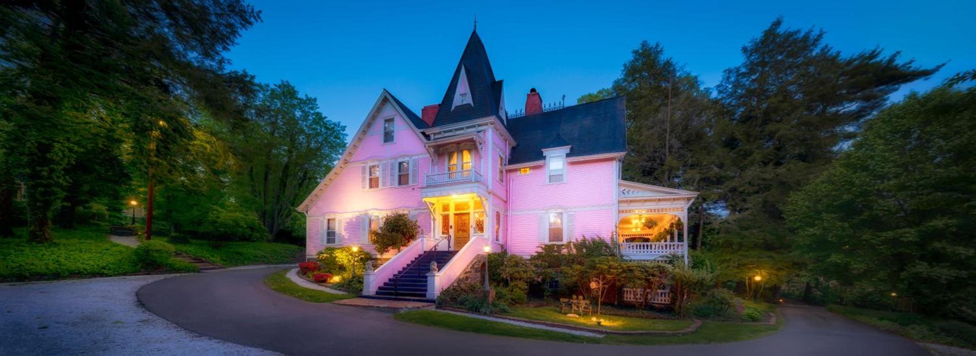 The Cedar Crest Inn, a pink Queen Anne Victorian mansion glowing at dusk, in Asheville, North Carolina
