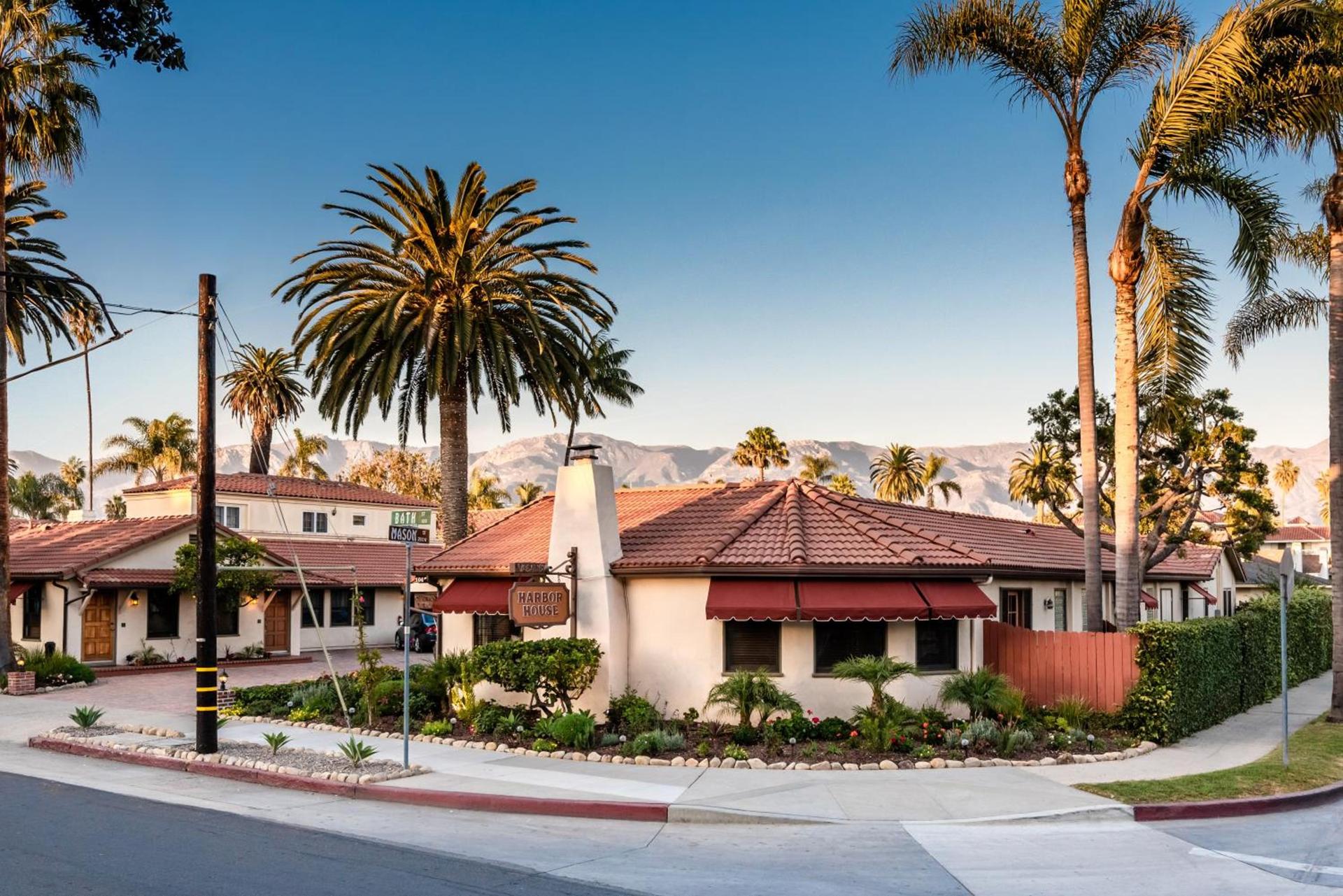 A red-tile-roofed Spanish-style inn framed by palms with the Santa Ynez Mountains behind it in Santa Barbara, California
