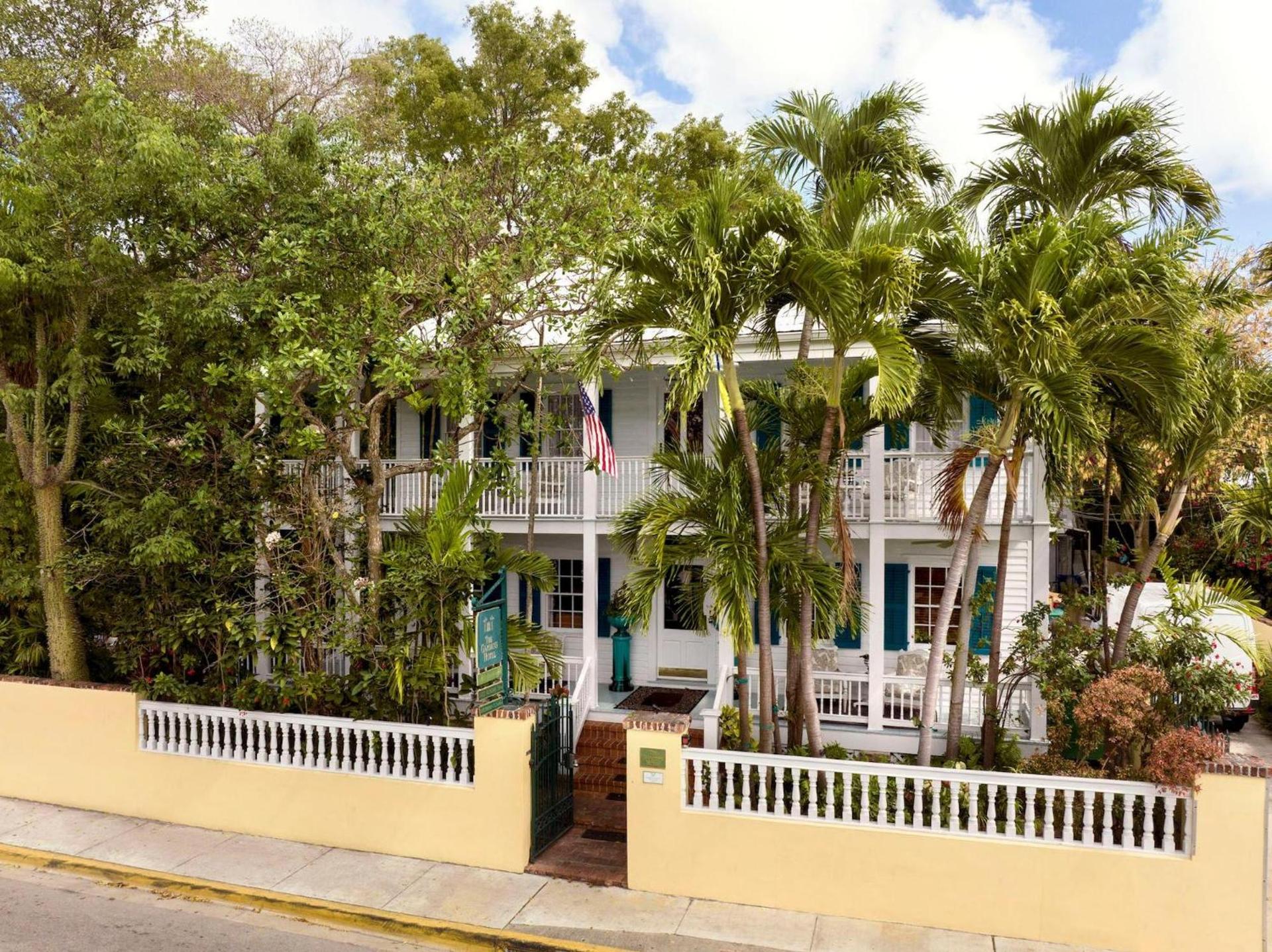 A historic white conch-house inn framed by palms and a yellow garden wall on a quiet Old Town street in Key West, Florida